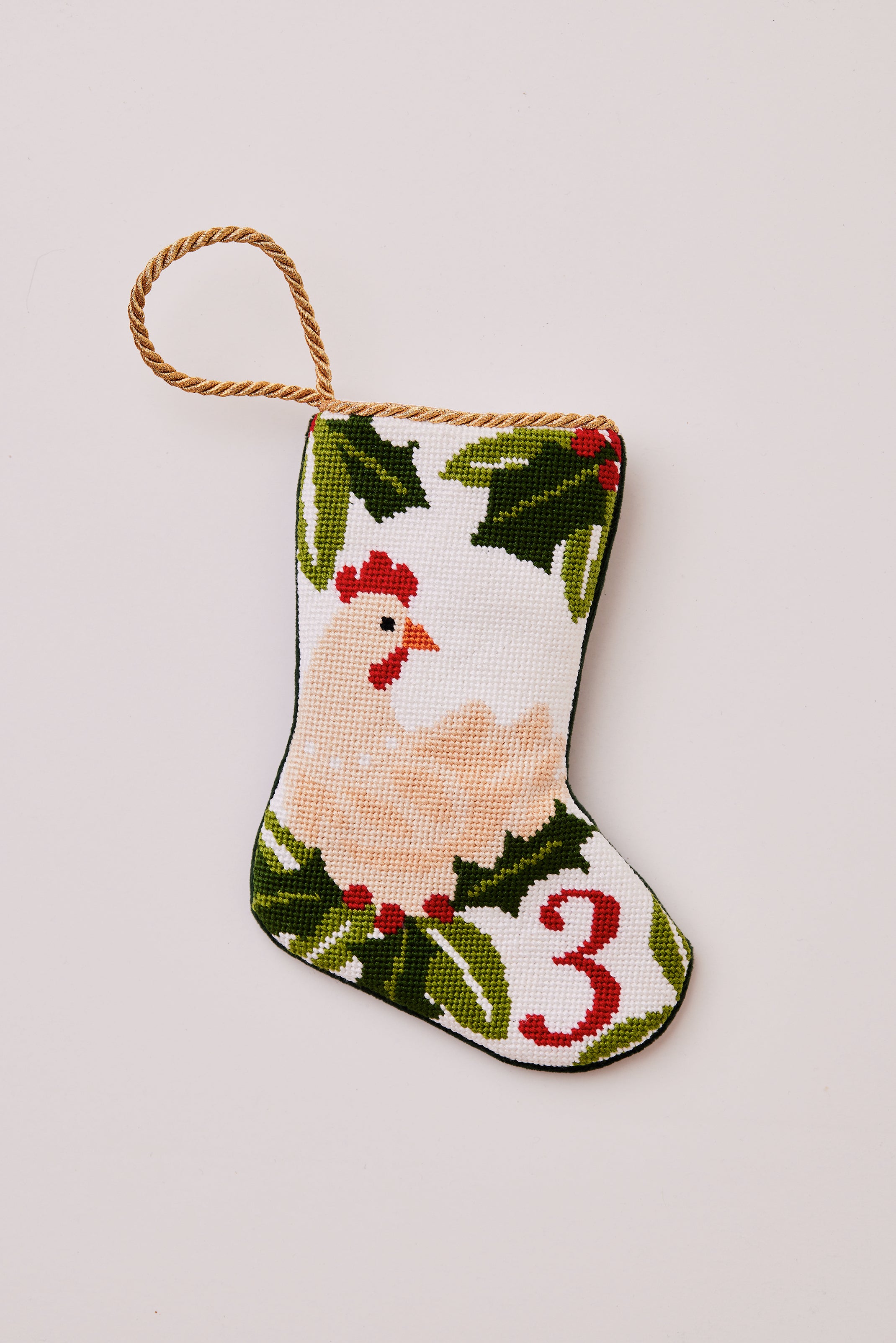 Needlepoint stocking featuring a hen with green holly accents on white backdrop