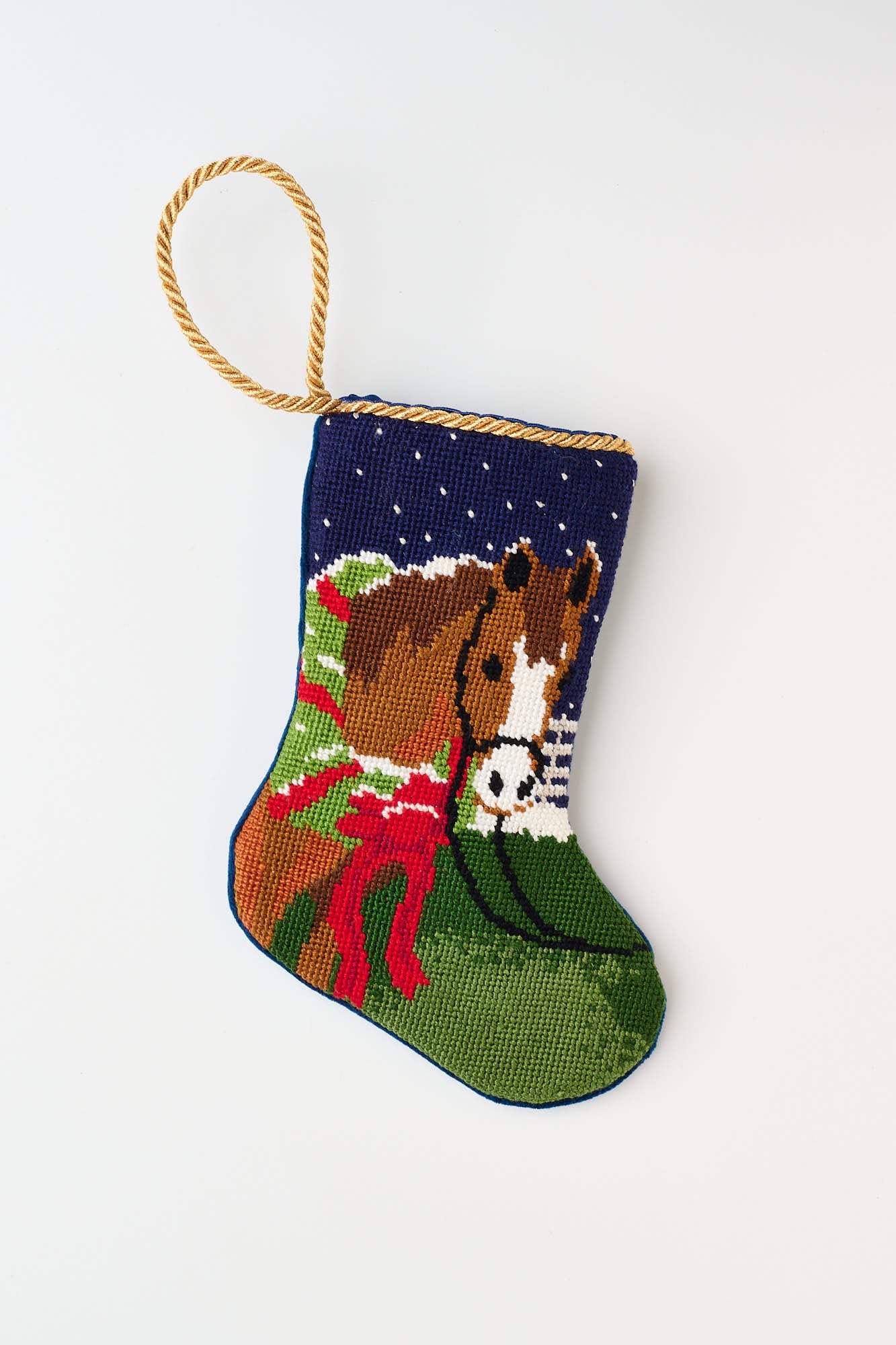 Hand-stitched needlepoint stocking featuring a horse with a red bow against a snowy blue background with a green meadow