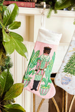 Full-size Christmas stocking featuring a vibrant nutcracker with festive details and palm accents on pink background