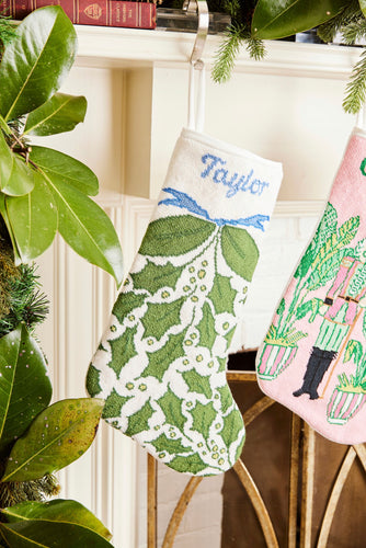 Full-size Christmas stocking with a monogrammed name in script featuring a vibrant greenery, holly, and decorative accents in festive shades of green and white