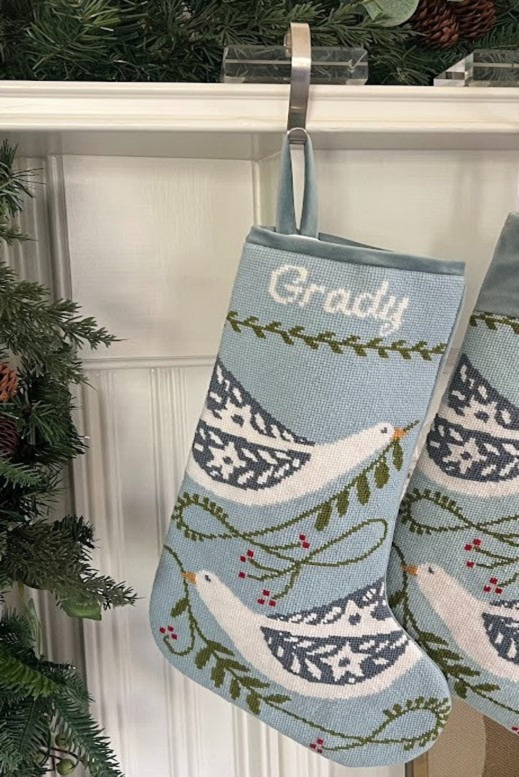 Full-size Christmas stocking with a monogrammed name in script featuring a white dove and greenery accents on a soft blue background