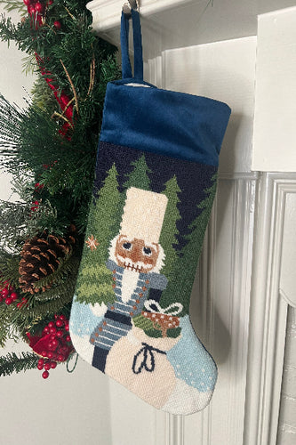 Full-size Christmas stocking featuring a Nutcracker holding a sack of gifts, standing on snowy ground, with trees in the background