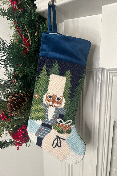 Full-size Christmas stocking featuring a Nutcracker holding a sack of gifts, standing on snowy ground, with trees in the background
