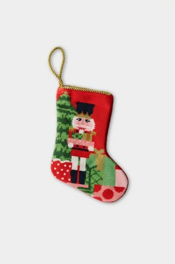 Hand-stitched needlepoint stocking with red-suited nutcracker and wrapped gifts on festive red background