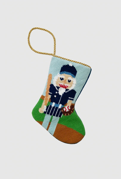 Needlepoint stocking featuring baseball nutcracker holding bat, glove, and ball on green field