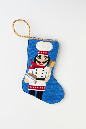 Needlepoint hand-stitched stocking with nutcracker chef wearing a uniform and toque, set against blue background.