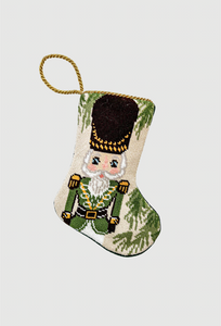 Hand-stitched needlepoint stocking featuring a nutcracker in green uniform with gold details and festive green accents