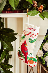 Full-size Christmas stocking with a monogrammed name in block featuring a red cardinal perched among holly, pinecones, and festive greenery