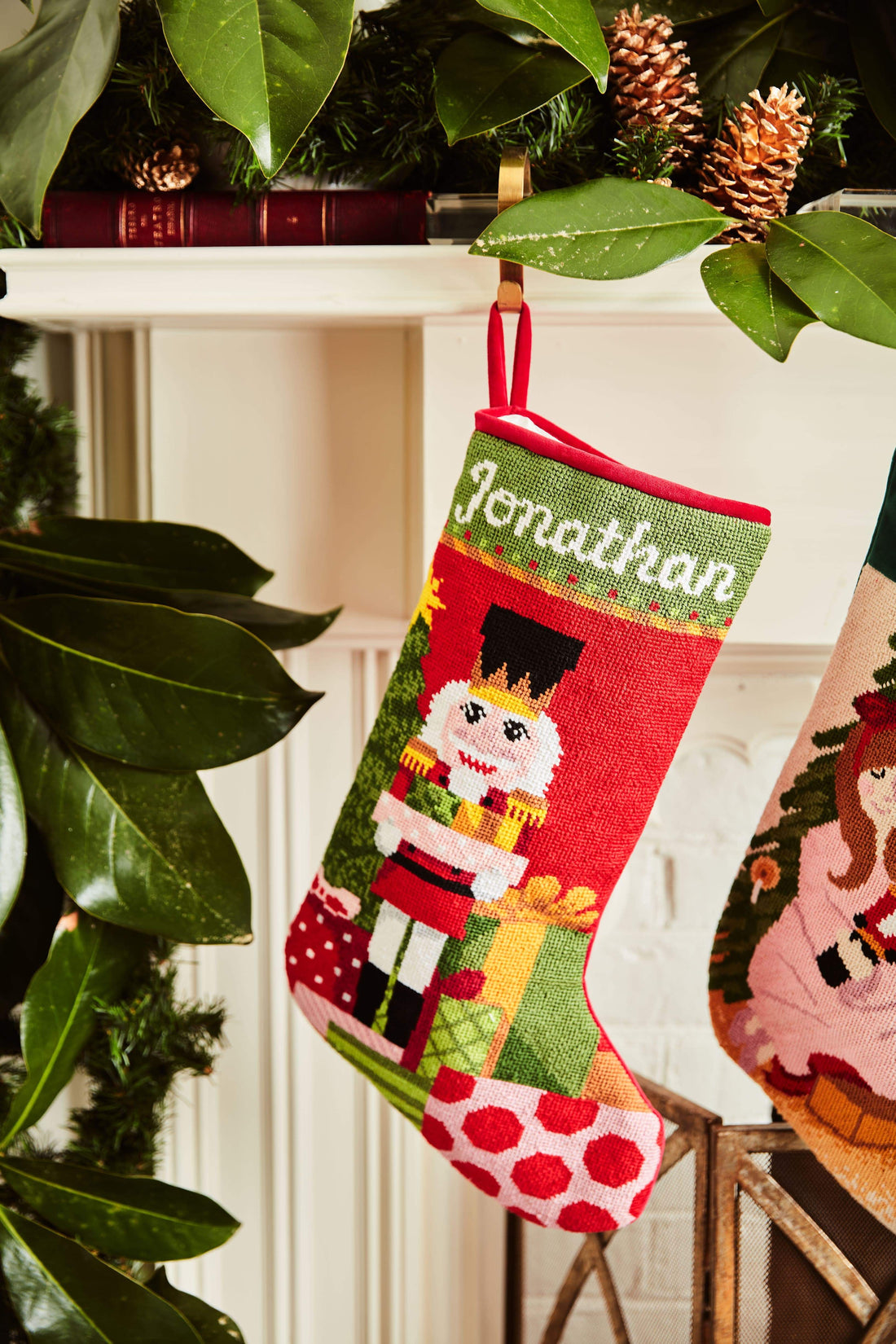 Full-size Christmas stocking with a monogrammed name in script featuring a red-suited nutcracker and wrapped gifts on festive red background