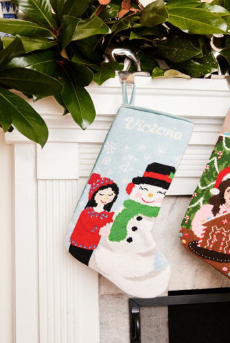 Full-size Christmas stocking with a monogrammed name in script featuring a smiling snowman and girl in red coat against snowy blue backdrop