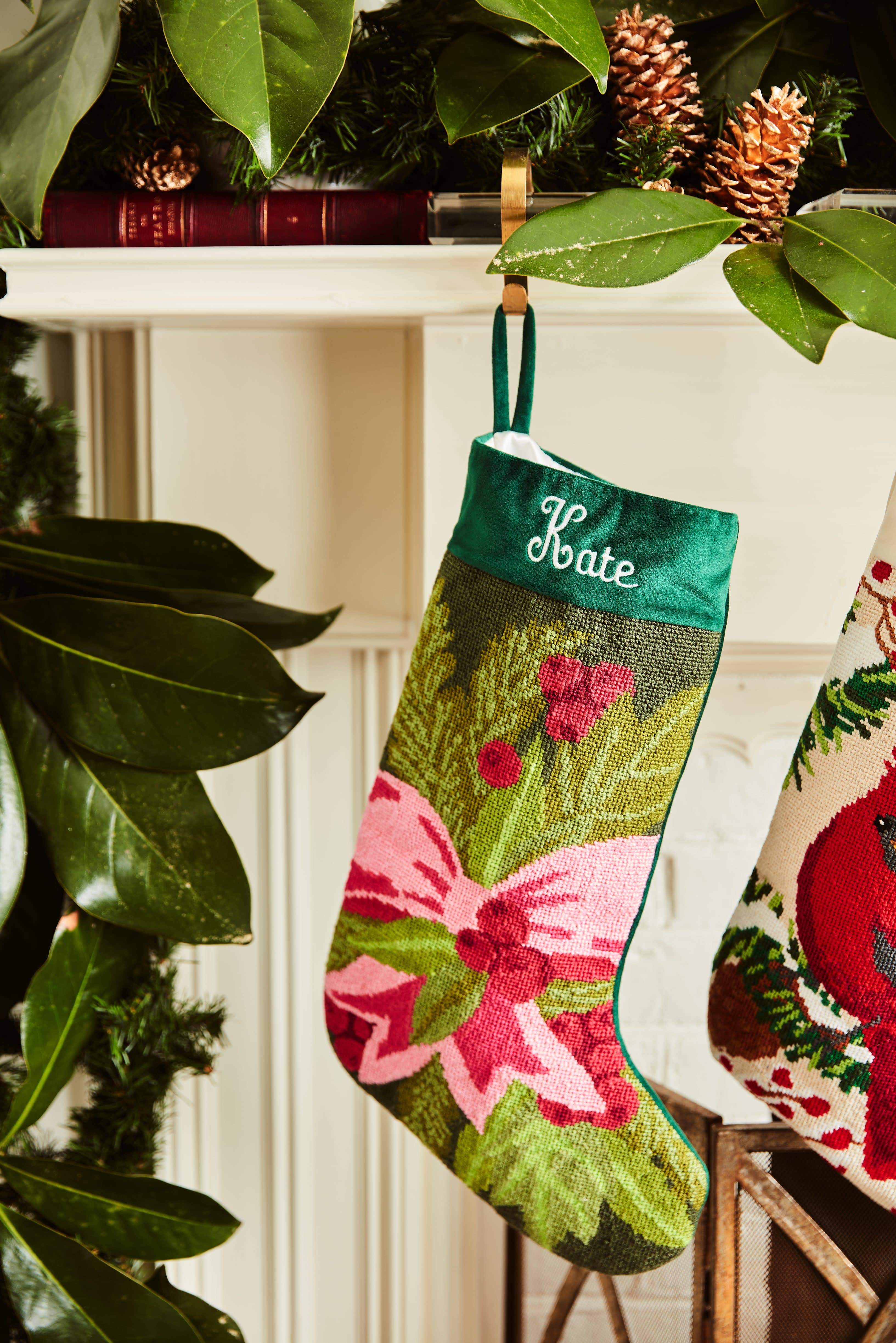 Full-size Christmas stocking with a monogrammed name in script featuring a pink bow with holly and pine branches on a green backdrop