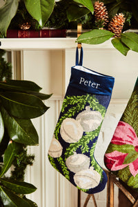 Full-size Christmas stocking with a monogrammed name in block featuring a silver bells and green garland on navy blue background