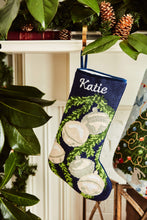 Full-size Christmas stocking with a monogrammed name in script featuring a silver bells and green garland on navy blue background