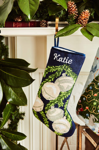 Full-size Christmas stocking with a monogrammed name in script featuring a silver bells and green garland on navy blue background
