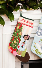Full-size Christmas stocking with a monogrammed name in script featuring a girl holding a nutcracker beside a Christmas tree and presents