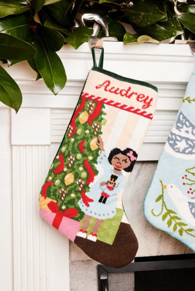 Full-size Christmas stocking with a monogrammed name in script featuring a girl holding a nutcracker beside a Christmas tree and presents
