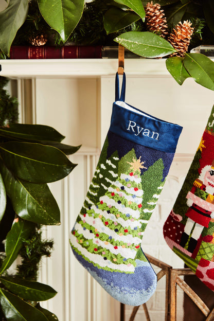 Full-size Christmas stocking with a monogrammed name in block featuring a snow-covered Christmas trees on a navy blue backdrop