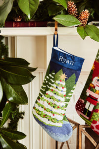 Full-size Christmas stocking with a monogrammed name in block featuring a snow-covered Christmas trees on a navy blue backdrop