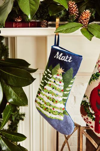 Full-size Christmas stocking with a monogrammed name in script featuring a snow-covered Christmas trees on a navy blue backdrop