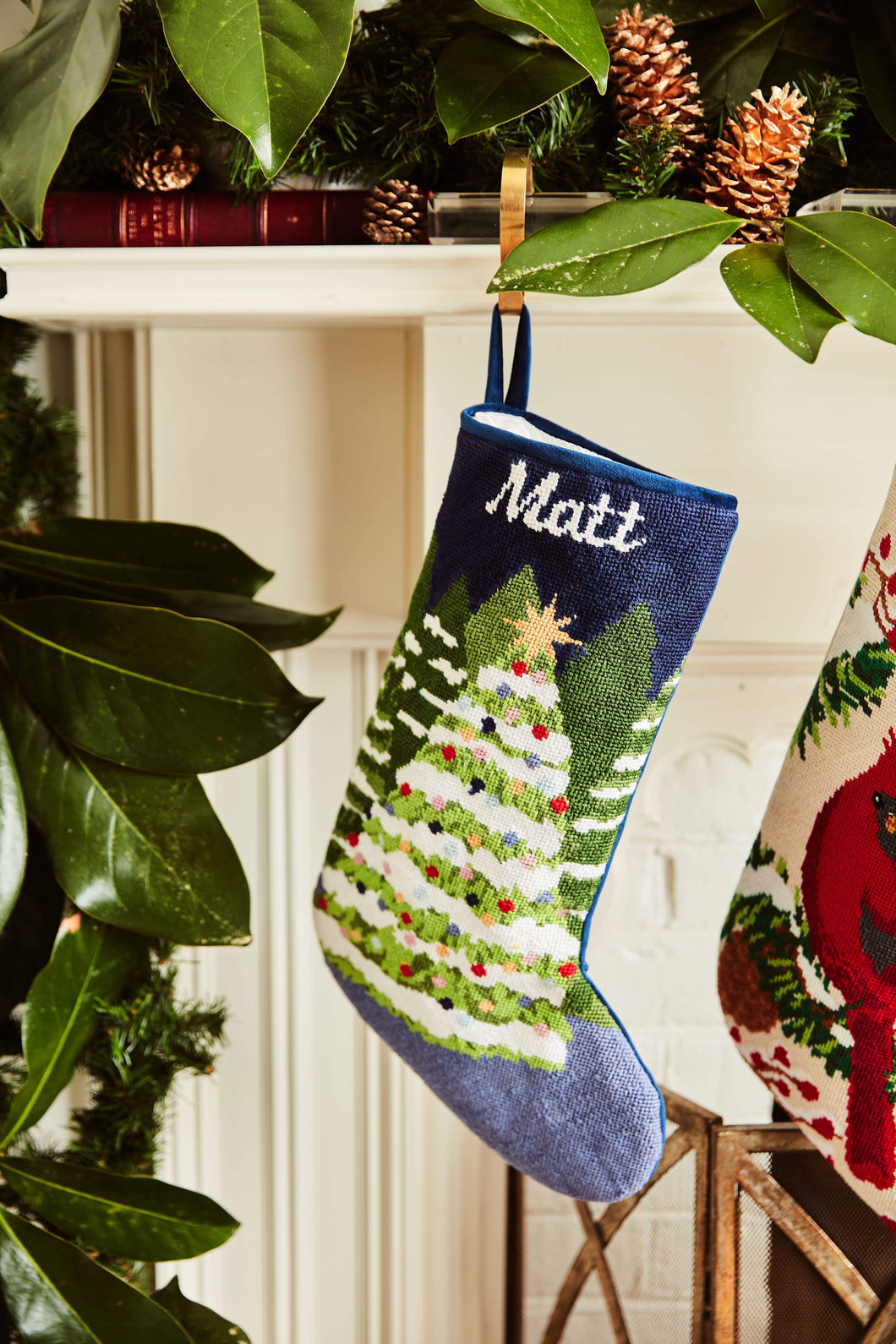 Full-size Christmas stocking with a monogrammed name in script featuring a snow-covered Christmas trees on a navy blue backdrop