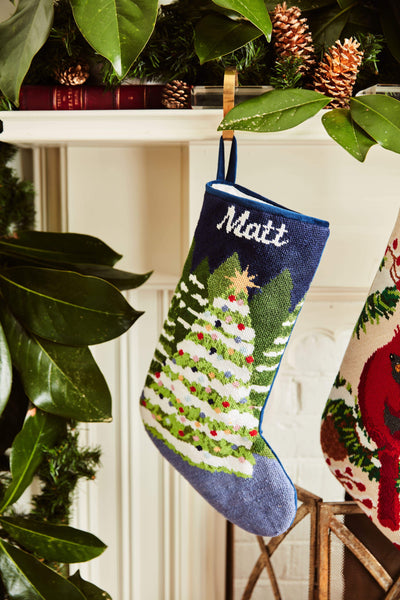 Full-size Christmas stocking with a monogrammed name in script featuring a snow-covered Christmas trees on a navy blue backdrop