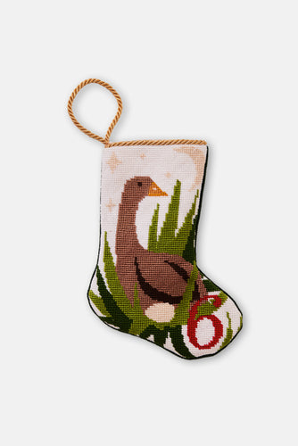Needlepoint stocking with goose nesting beside an egg and grass under a starry sky on blush background