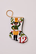 Hand-stitched Christmas stocking featuring drummer in green coat with yellow hat surrounded by greenery on white background