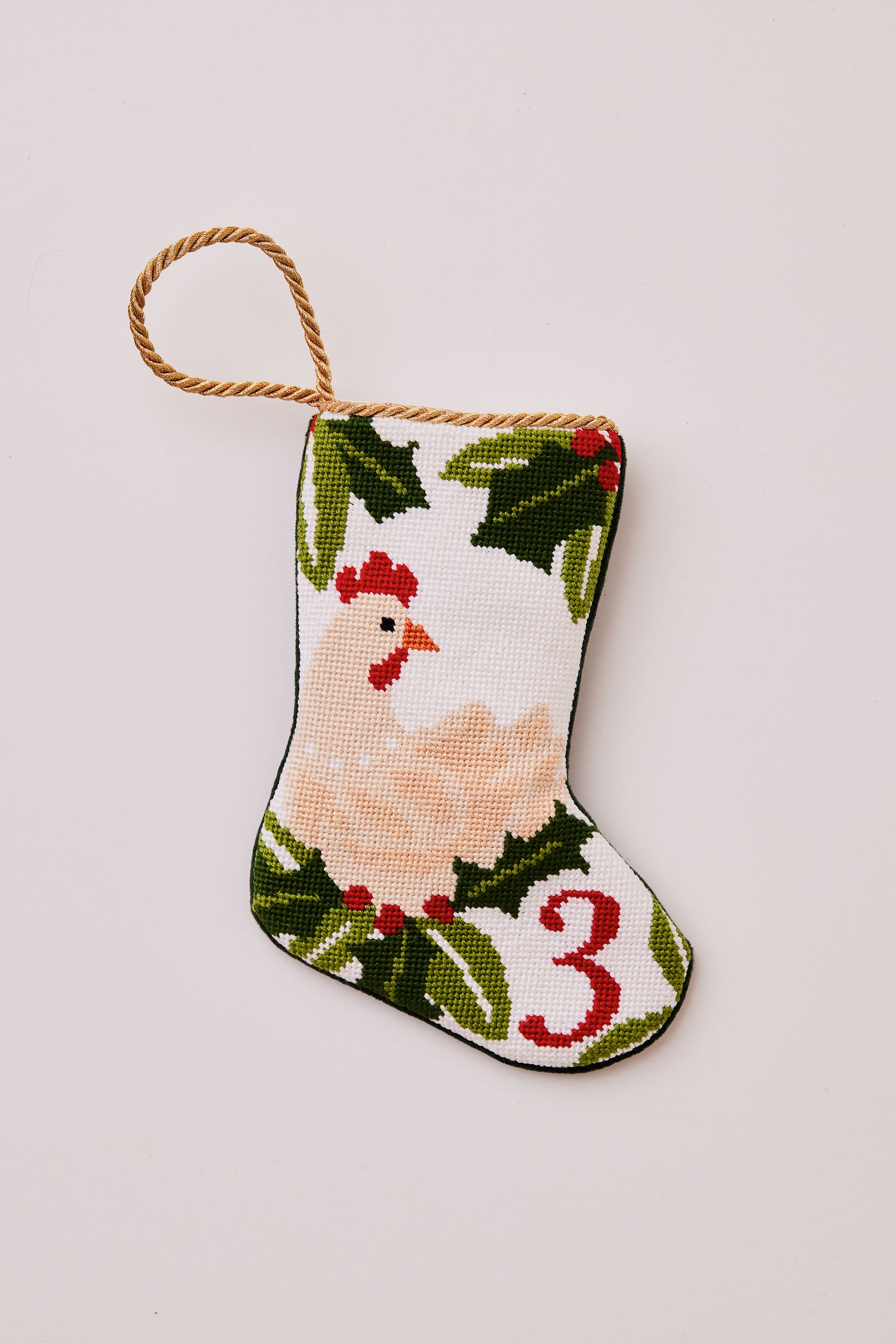 Needlepoint stocking featuring a hen with green holly accents on white backdrop