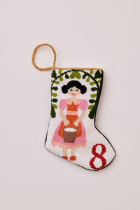 Hand-stitched stocking featuring milkmaid in pink and orange holding a pail, with greenery on a white backdrop
