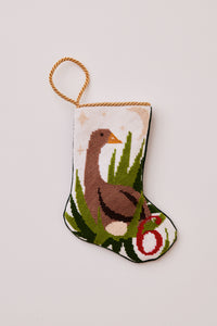 Needlepoint stocking with goose nesting beside an egg and grass under a starry sky on blush background