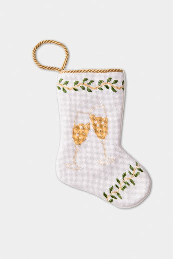 Hand-stitched needlepoint stocking featuring two champagne glasses clinking against a backdrop of greenery on a white background