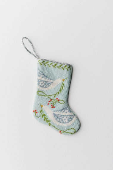 Hand-stitched needlepoint stocking with white dove and greenery accents on a soft blue background