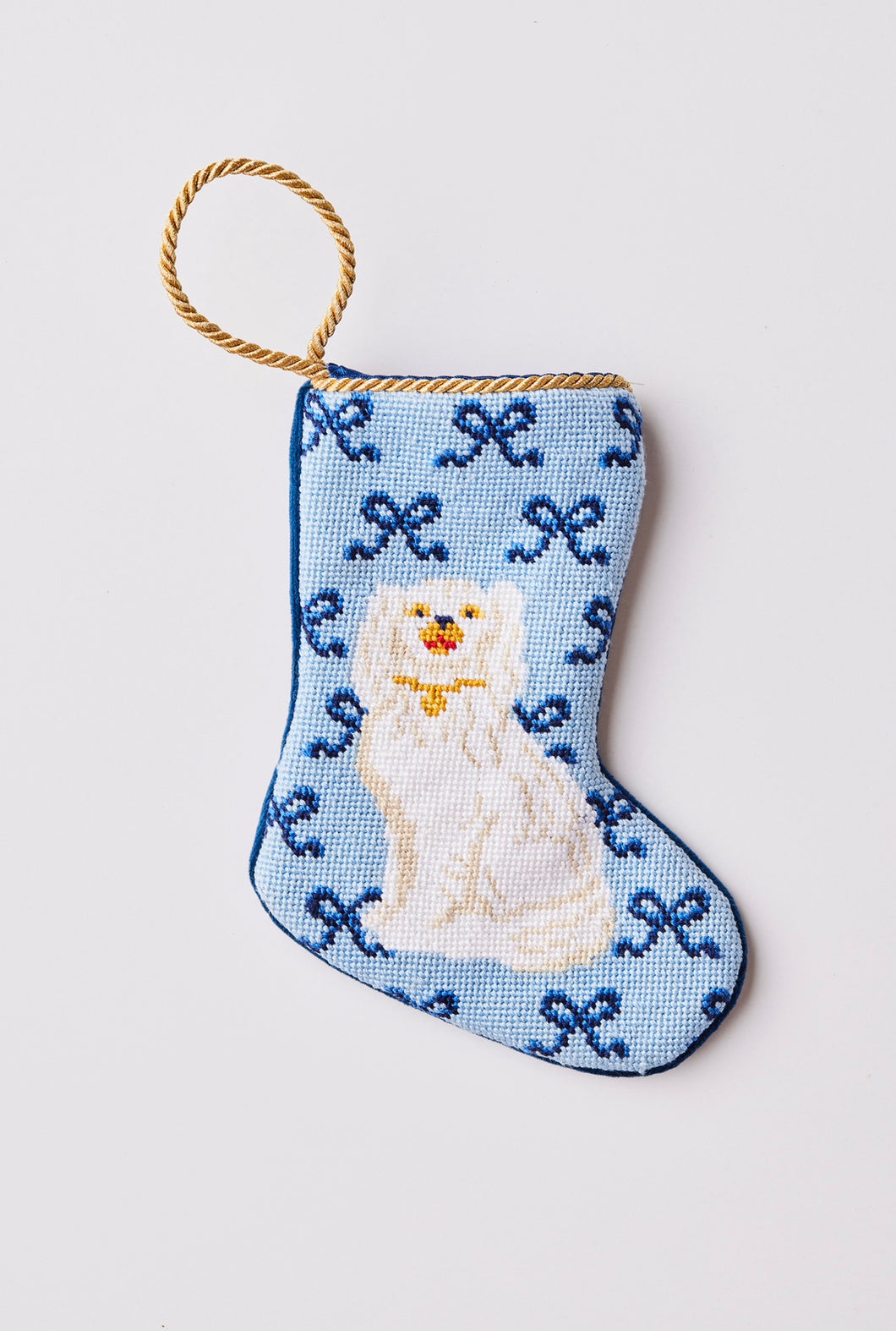 Hand-stitched needlepoint stocking featuring a white dog sitting with bows on a blue backdrop